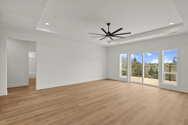 unfurnished room with light wood-style flooring, a tray ceiling, and baseboards