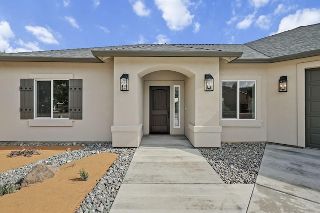 property entrance featuring a shingled roof and stucco siding