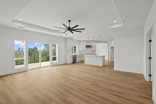 unfurnished living room with ceiling fan, recessed lighting, baseboards, light wood-style floors, and a raised ceiling