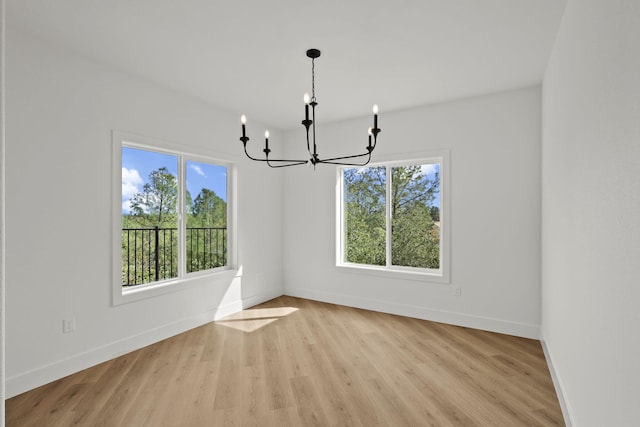 unfurnished dining area with baseboards, light wood finished floors, and an inviting chandelier