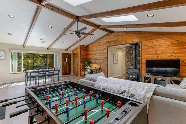 recreation room featuring recessed lighting, a wood stove, wood walls, ceiling fan, and vaulted ceiling with skylight