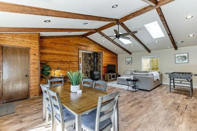 18260 Racoon Dr, Lakehead, CA 96051 - dining room featuring vaulted ceiling with skylight, light wood-style flooring, wood walls, a ceiling fan, and a wood stove