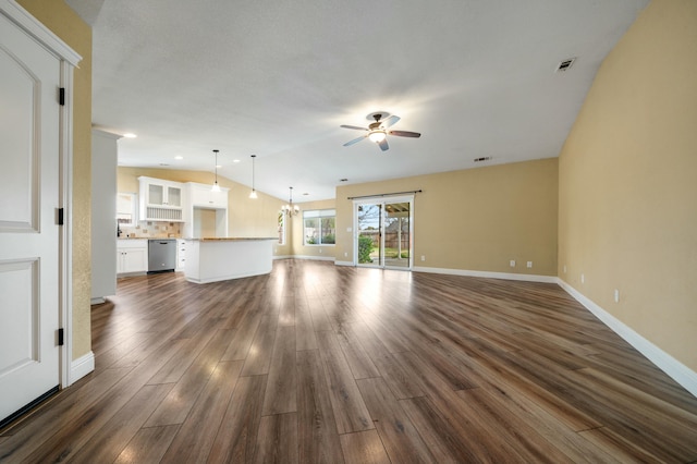 unfurnished living room with lofted ceiling, ceiling fan with notable chandelier, visible vents, baseboards, and dark wood finished floors