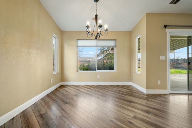 unfurnished dining area with visible vents, a notable chandelier, baseboards, and wood finished floors