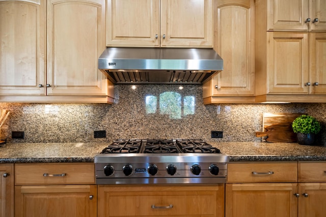 kitchen with light brown cabinets, under cabinet range hood, tasteful backsplash, dark stone countertops, and stainless steel gas stovetop