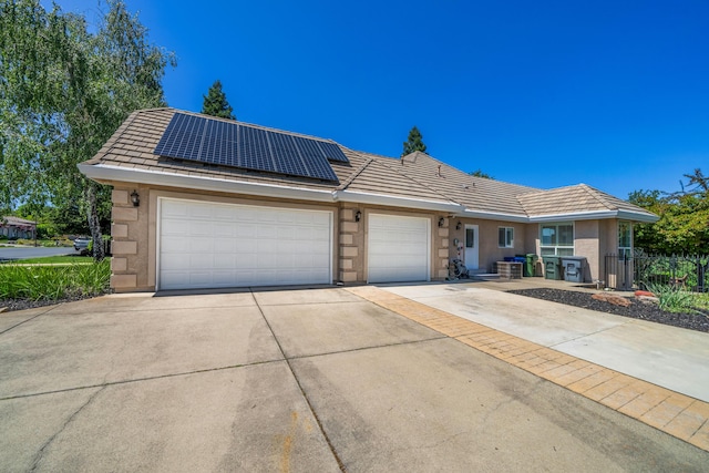 view of front of home featuring driveway, a tiled roof, an attached garage, roof mounted solar panels, and stucco siding