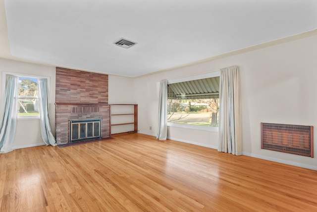 unfurnished living room featuring a fireplace, heating unit, visible vents, light wood-type flooring, and baseboards
