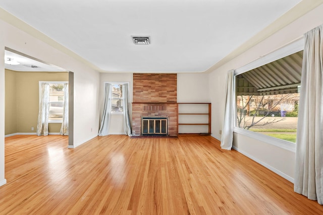 unfurnished living room featuring a brick fireplace, light wood-style flooring, visible vents, and baseboards