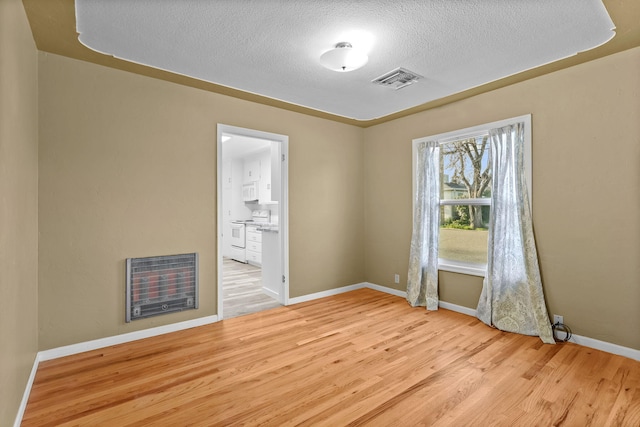 unfurnished room with baseboards, visible vents, wood finished floors, heating unit, and a textured ceiling