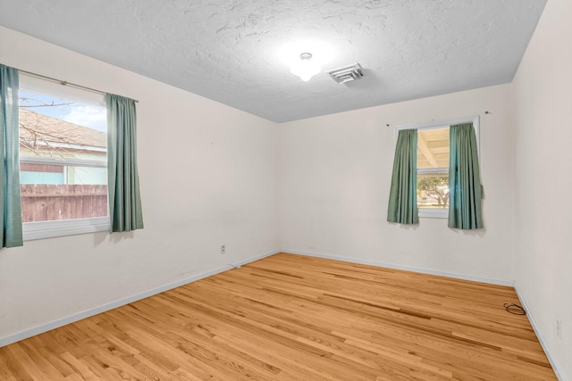 empty room with a textured ceiling, wood finished floors, visible vents, and baseboards