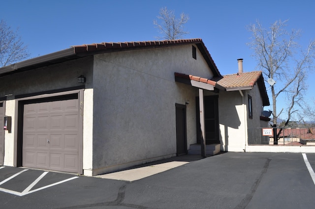 view of side of home featuring a garage, stucco siding, and a tiled roof