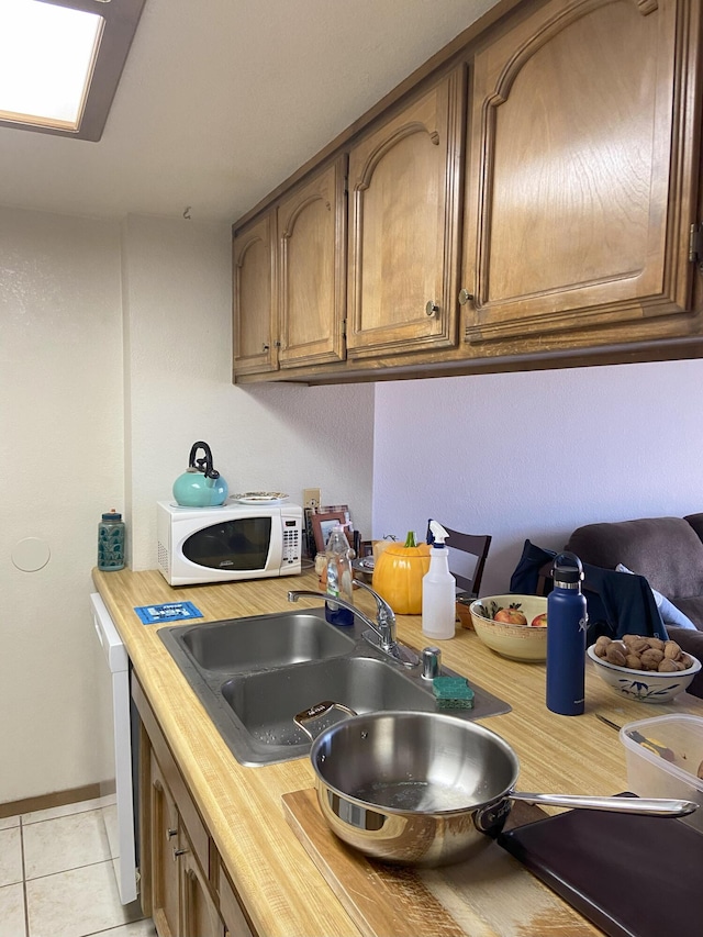 kitchen with light tile patterned floors, light countertops, white microwave, brown cabinetry, and a sink