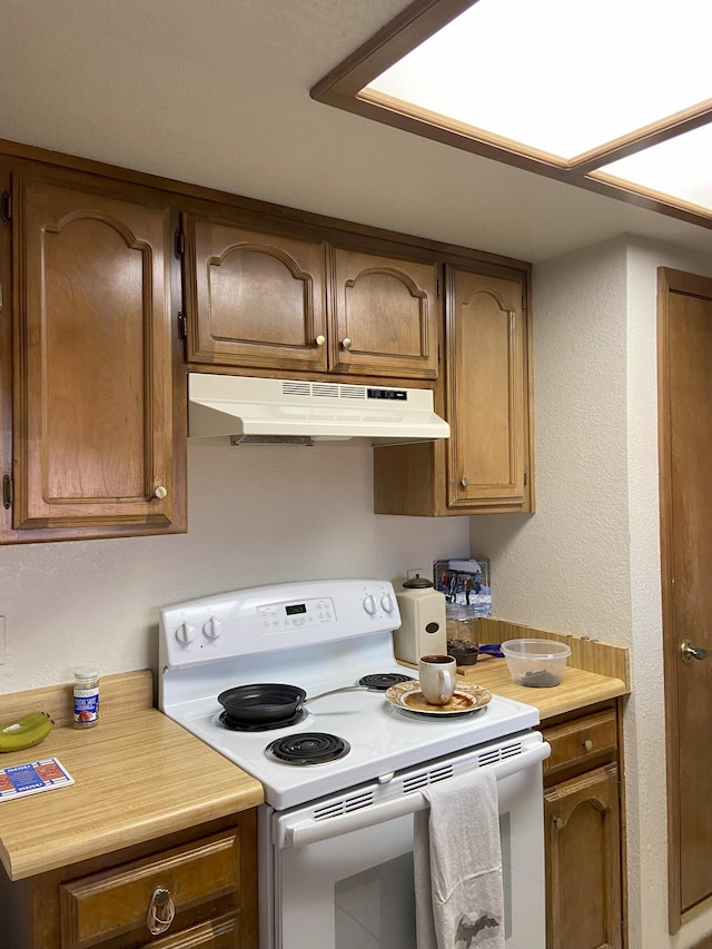 kitchen with under cabinet range hood, light countertops, white electric range, and a textured wall