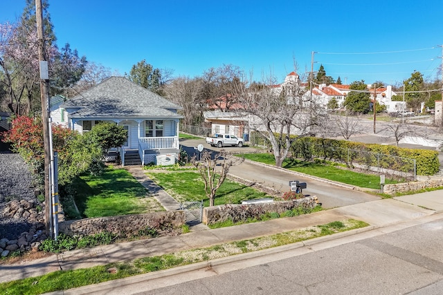 view of front of home with driveway, a shingled roof, a fenced front yard, a porch, and a front lawn