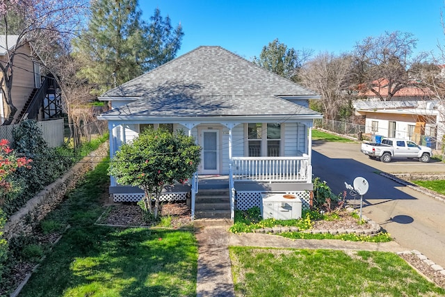 bungalow-style house with a shingled roof, covered porch, fence, and a front lawn