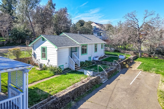 view of front of house with central AC, a shingled roof, a front yard, and a garden