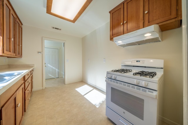 kitchen with white gas stove, under cabinet range hood, visible vents, light countertops, and brown cabinetry