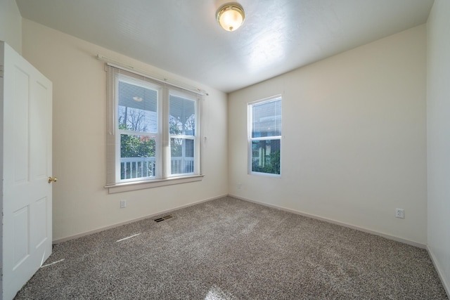 carpeted empty room featuring a wealth of natural light, visible vents, and baseboards