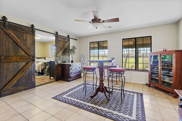 dining area featuring light tile patterned floors, ceiling fan, a barn door, and a textured ceiling