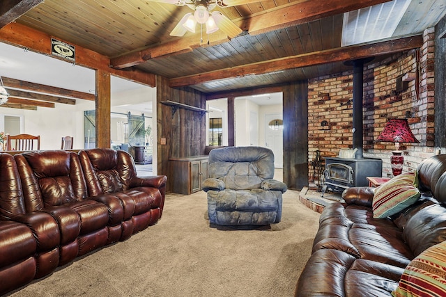 living area featuring ceiling fan, a barn door, beam ceiling, carpet, and a wood stove