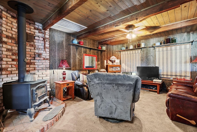 carpeted living area with a ceiling fan, a wood stove, wooden ceiling, and beamed ceiling