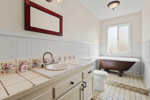 full bath with a wainscoted wall, toilet, vanity, a freestanding tub, and tile patterned floors