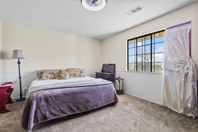 carpeted bedroom featuring a wainscoted wall, a textured ceiling, and visible vents