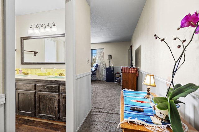 hallway featuring a textured ceiling, dark colored carpet, wainscoting, and a sink