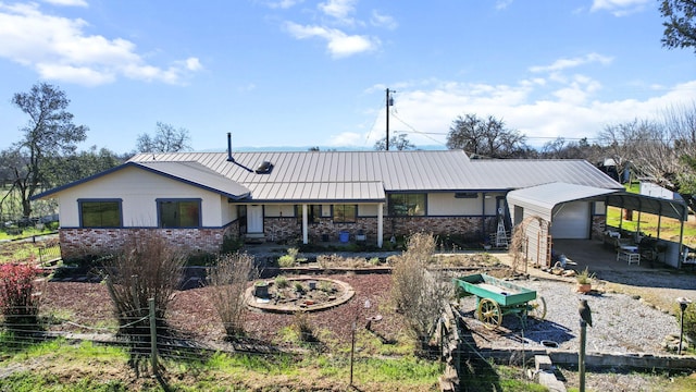 back of house featuring brick siding, a standing seam roof, metal roof, stone siding, and driveway