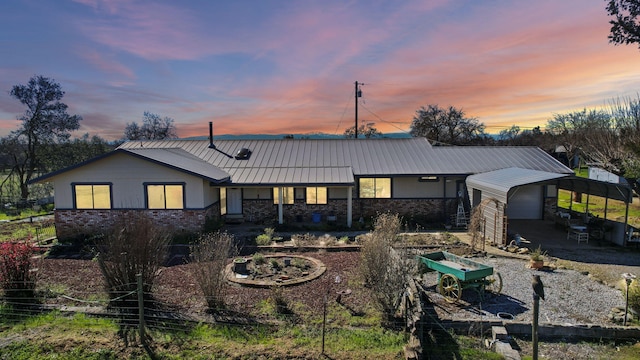 rear view of property featuring metal roof, stone siding, driveway, a carport, and a standing seam roof