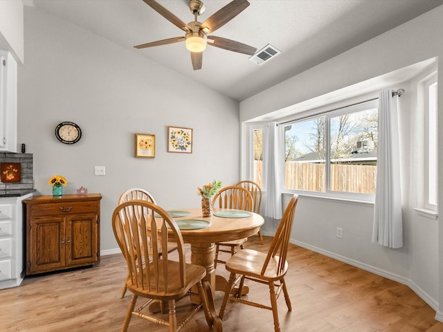 dining space featuring visible vents, baseboards, light wood-style flooring, and vaulted ceiling