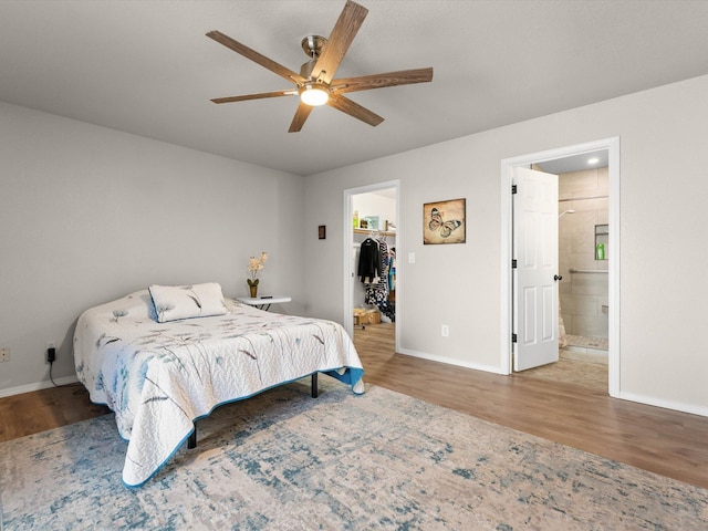 bedroom featuring a walk in closet, wood finished floors, baseboards, and connected bathroom