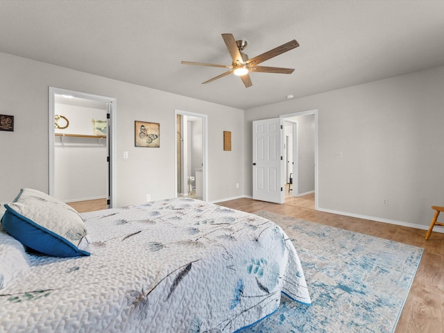 bedroom with wood finished floors, baseboards, a ceiling fan, ensuite bathroom, and a walk in closet