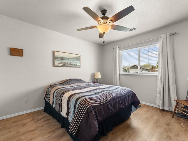 bedroom with a ceiling fan, wood finished floors, visible vents, baseboards, and a textured ceiling