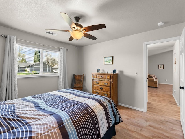 bedroom featuring visible vents, baseboards, light wood-style flooring, a textured ceiling, and a ceiling fan