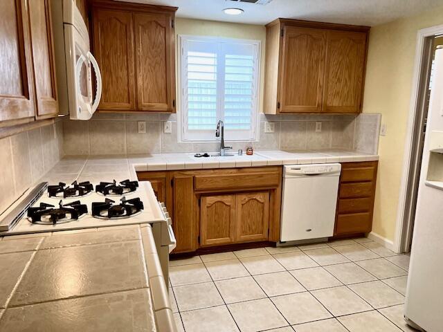 kitchen featuring brown cabinets, tile countertops, tasteful backsplash, a sink, and white appliances