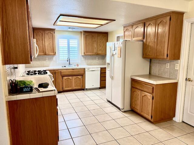 kitchen featuring tasteful backsplash, tile counters, brown cabinetry, a sink, and white appliances