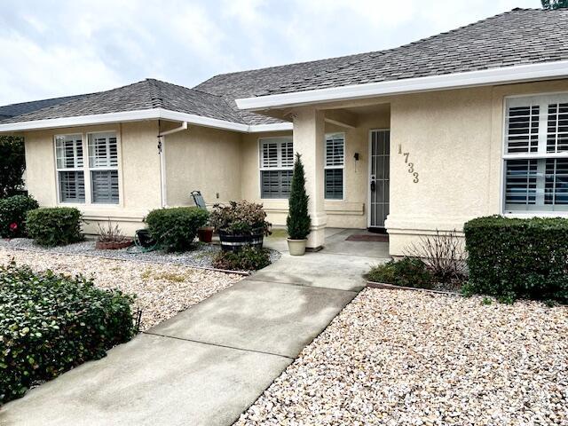 view of exterior entry with a shingled roof and stucco siding