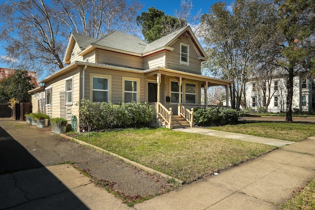 view of front facade with covered porch, roof with shingles, and a front lawn