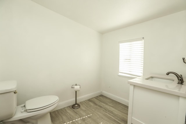 half bath with vanity, wood finished floors, toilet, and baseboards