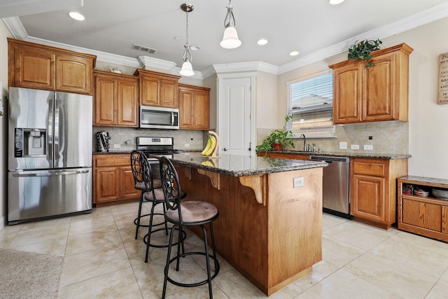 kitchen featuring visible vents, a kitchen island, brown cabinets, stainless steel appliances, and a kitchen bar