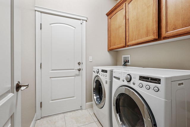 laundry room with light tile patterned floors, separate washer and dryer, cabinet space, and baseboards