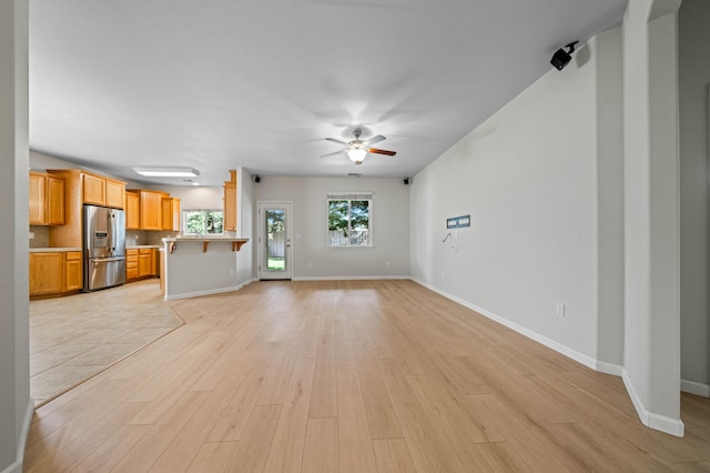 unfurnished living room featuring light wood finished floors, baseboards, and a ceiling fan