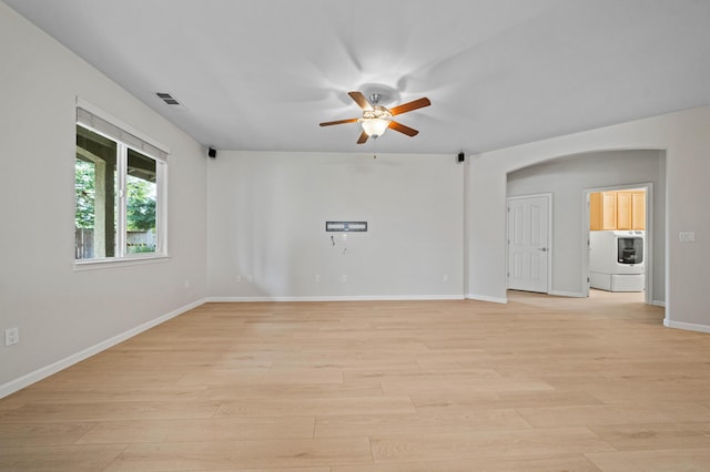 unfurnished room with baseboards, arched walkways, a ceiling fan, washer / clothes dryer, and light wood-type flooring