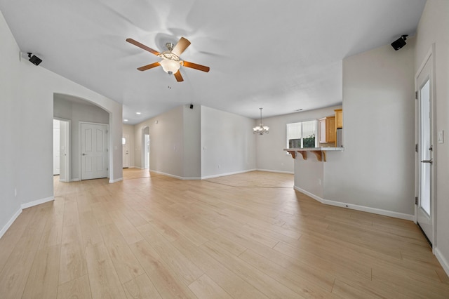 unfurnished living room with arched walkways, baseboards, light wood finished floors, and ceiling fan with notable chandelier