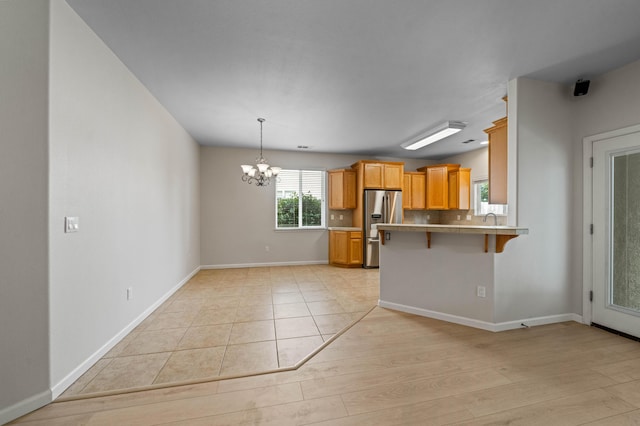 kitchen featuring stainless steel fridge, a breakfast bar area, a peninsula, an inviting chandelier, and light countertops