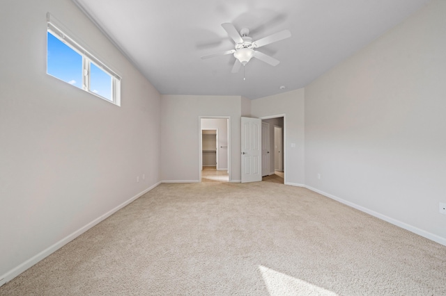 unfurnished bedroom with baseboards, a spacious closet, a ceiling fan, and light colored carpet