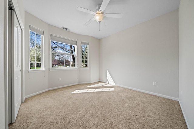 carpeted empty room with ceiling fan, visible vents, and baseboards