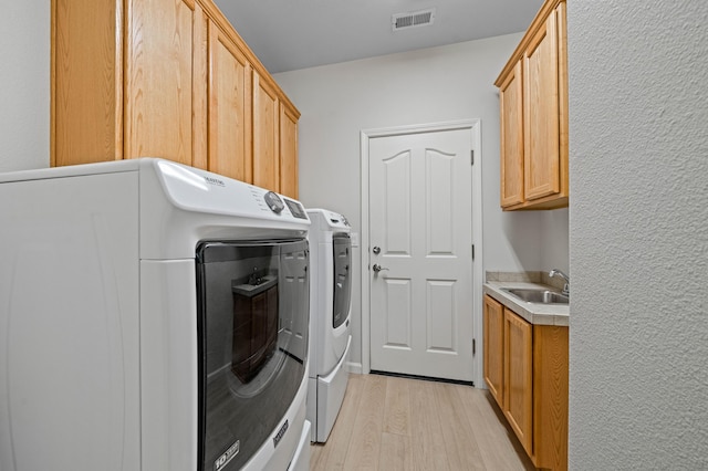 laundry room with light wood-style flooring, separate washer and dryer, a sink, visible vents, and cabinet space