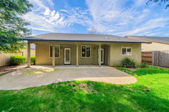 back of property featuring a yard, a patio, stucco siding, a shingled roof, and fence